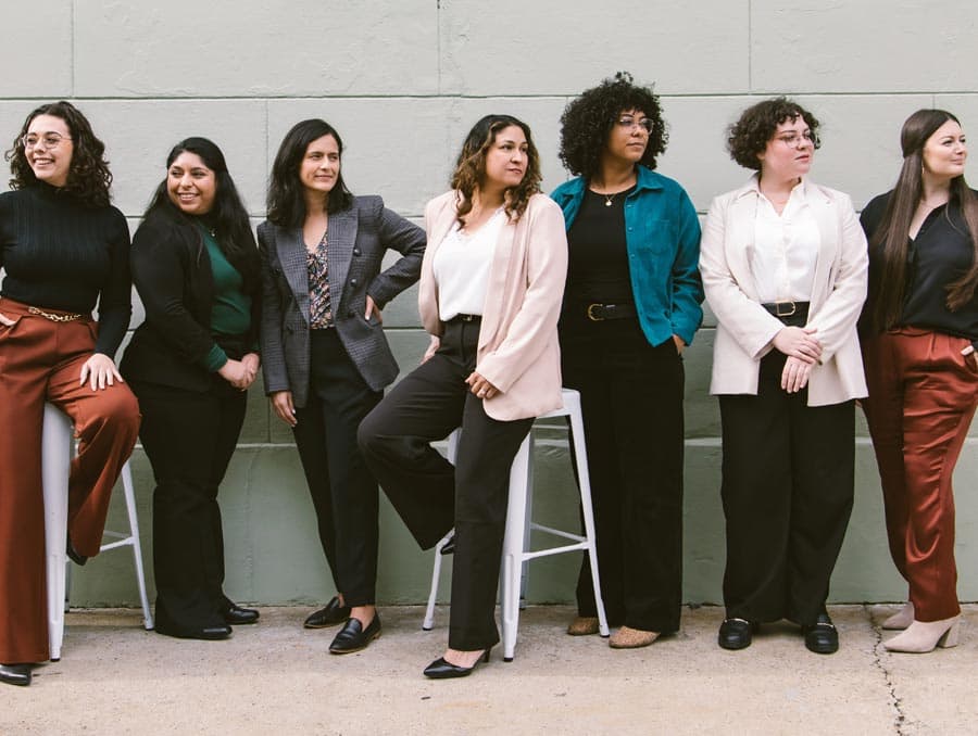 Seven Latina women wearing professional attire standing together